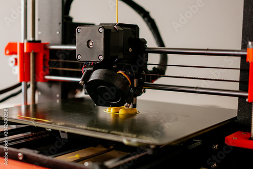 Tableau sur toile Close up of desktop 3D printer extruder head printing yellow plastic model on a