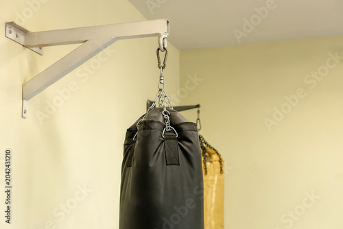Fotografie Black heavy punching bag hanging on a white steel wall bracket inside an empty m