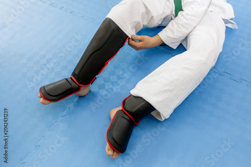 Fényképezés Cropped shot of youth martial arts fighter putting on black and red shin guards