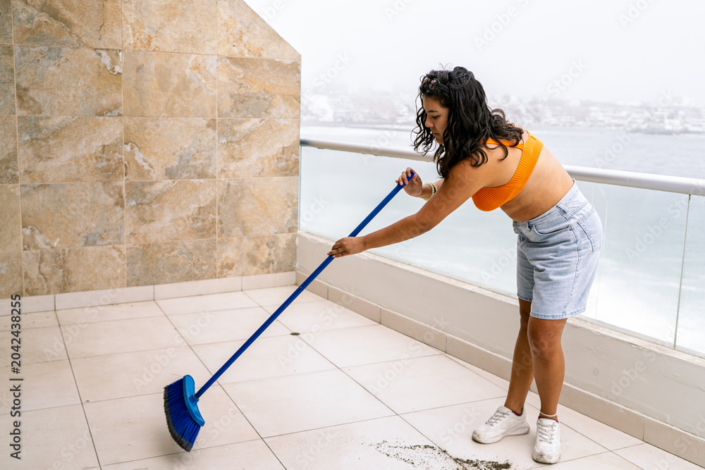 Obraz premium Woman sweeping beach house balcony, preparing for summer