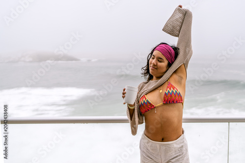 Photography Woman stretching with coffee on oceanfront balcony