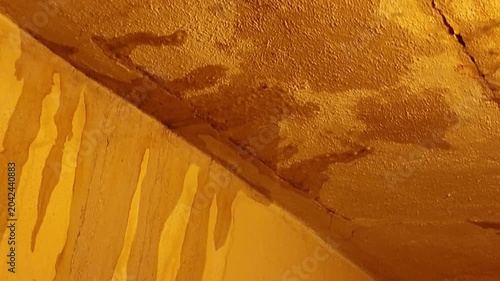 Close-up view of water stains and cracks on a textured yellow surface. Detailed texture of a yellow surface showing signs of water damage, including streaks and fissures, suggesting an aged or