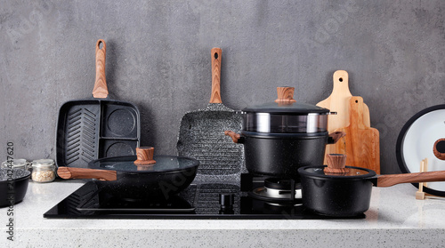 Modern black cookware set with wooden handles on kitchen stovetop