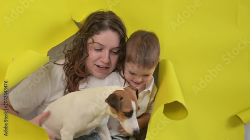 Caucasian little boy, his mother and Jack Russell Terrier dog tearing yellow paper background. 