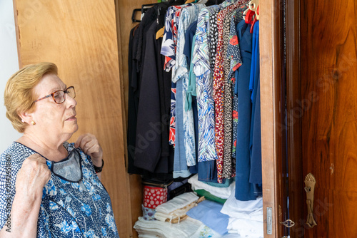 An older woman tries on a shirt while looking in the mirror.