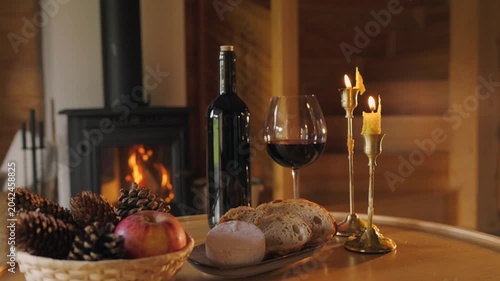 Slow living scene with wine, bread and candles by fireplace. Cozy interior