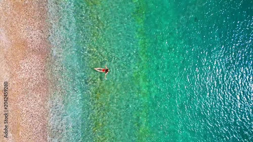 Woman in red swimsuit swims in the clear sea, top down view