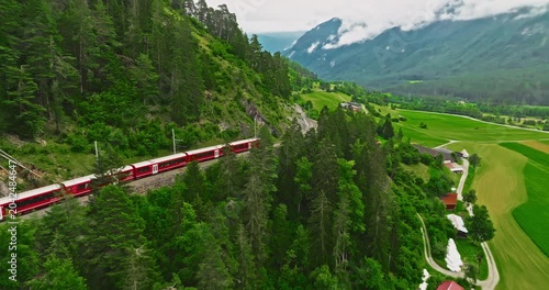 Aerial video of the red train traversing the Landwasser viaduct. The Swiss Express travels through the green meadows and mountains of Switzerland. Passenger transportation in Switzerland