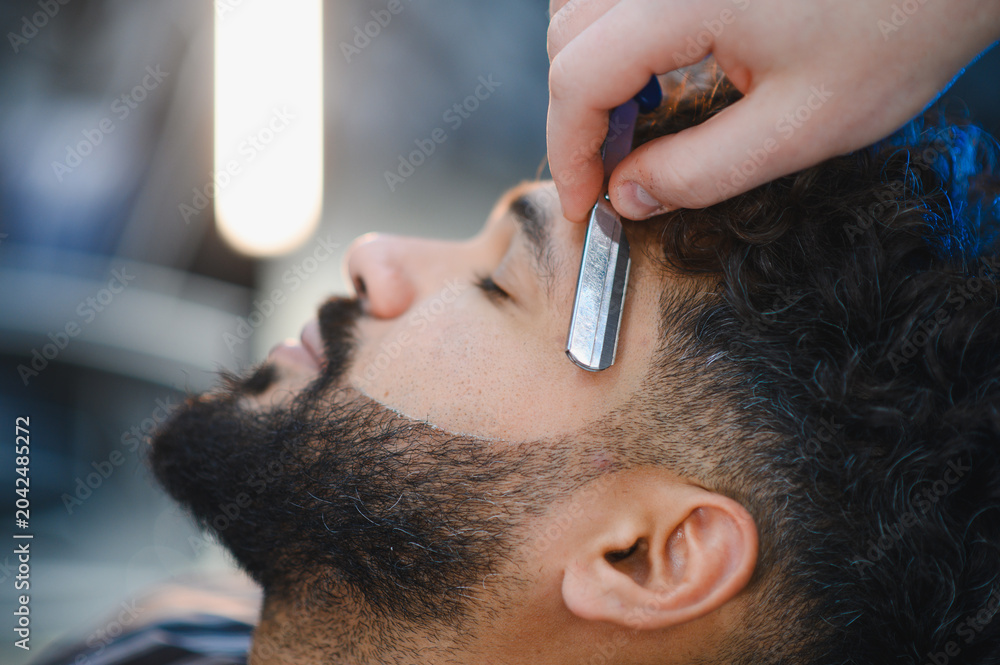 Fototapeta premium Barber shaving man's beard hairline with straight razor