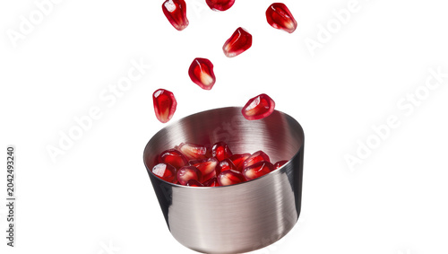 Fotografie Shiny metal bowl filled with fresh pomegranate seeds, some falling isolated on t