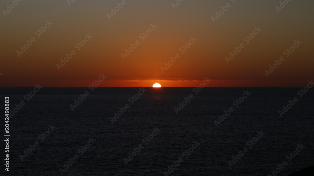 Fototapeta premium Sun dips low, painting sky in warm orange hues