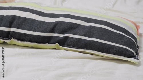 Striped pillow lying on white bed sheet