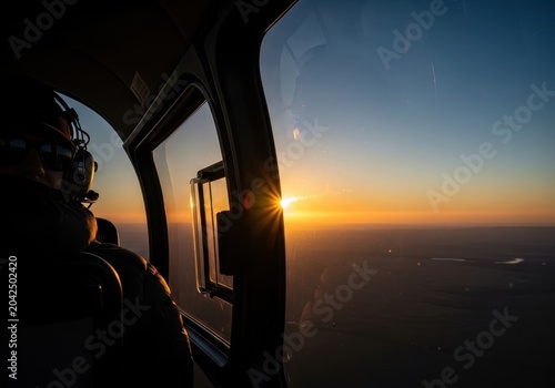 Scenic view from a helicopter at sunset, with a pilot looking out over the horizon and a bright sun flare