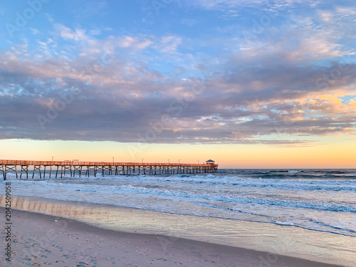 Εκτύπωση καμβά Soft morning light illuminates the Atlantic Beach fishing pier as waves roll onto the shore beneath colorful clouds along North Carolina’s Crystal Coast