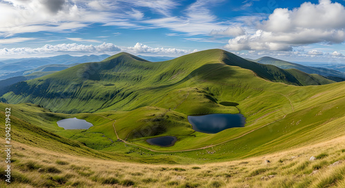 Panoramic view of green rolling mountain slopes and pristine glacial lakes under a bright blue sky with fluffy white clouds