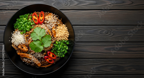 Delicious stir fried glass noodles served in a black bowl with fresh cilantro red chili peppers and crunchy chopped peanuts