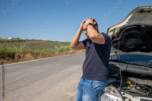 Foto Man standing by his broken down car with the hood open, holding his head in dist