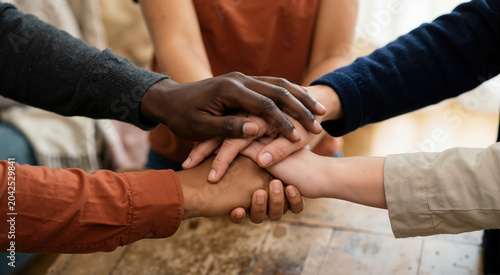 Close up of diverse hands intertwined and stacked together over a wooden table. Interracial solidarity and teamwork concept