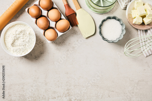 Bild auf Leinwand Top view of baking ingredients and kitchen utensils forming a border on a light stone background