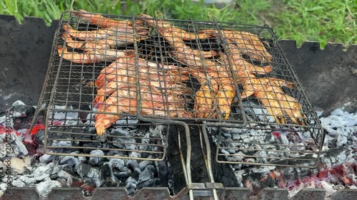 Fresh shrimp roasting on metal grill grate above burning charcoal during outdoor barbecue cooking with delicious seafood atmosphere in nature.
