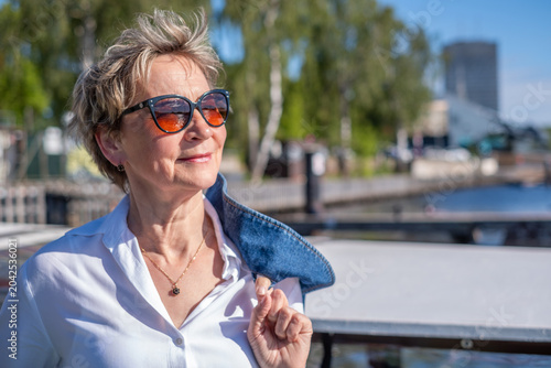 Elegant senior woman standing on marina pier looking into distance in sunshine, active retirement and luxury travel lifestyle concept in spring and summer with copy space
