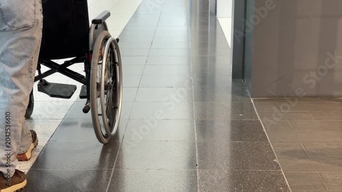 A faceless woman pushes a wheelchair through a shopping mall.