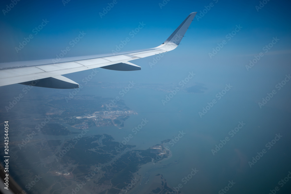 Fototapeta premium Airplane wing flying over the blue ocean coastline with islands.