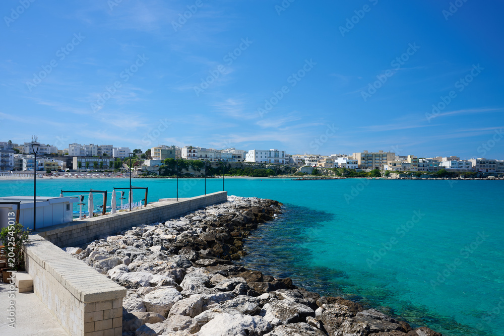 Fototapeta premium View over seawall \ groyne \ harbour wall \ harbor wall with no boats on turquoise sea under blue sky