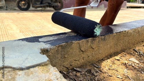 Cuadro en lienzo Man applying black paint to concrete curb with a paint roller