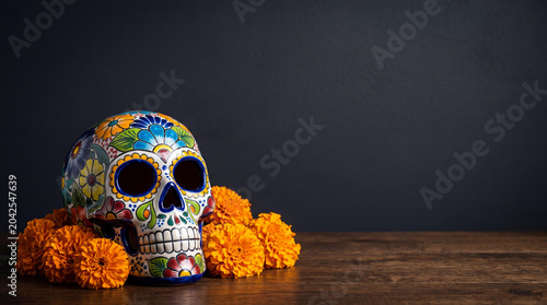 Calavera decorated skull on wooden surface with cempasuchil flower. Traditional folk art for celebration of Day of the Dead. Mexican cultural symbol for holiday memorial of ancestor.