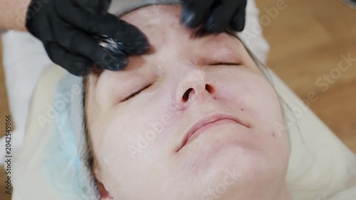 A female professional cosmetologist applies protective ointment to a client after a procedure
