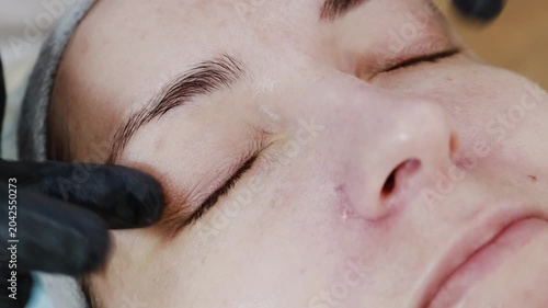 A female professional cosmetologist applies protective ointment to a client after a procedure