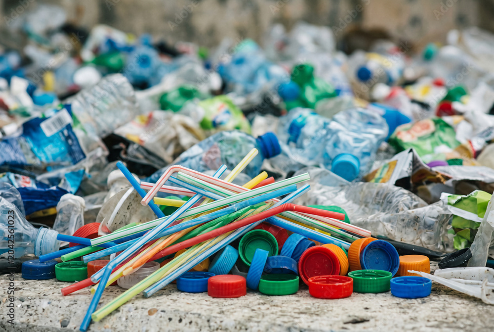 Fototapeta premium Pile of colorful single use plastic straws and bottle caps in garbage dump