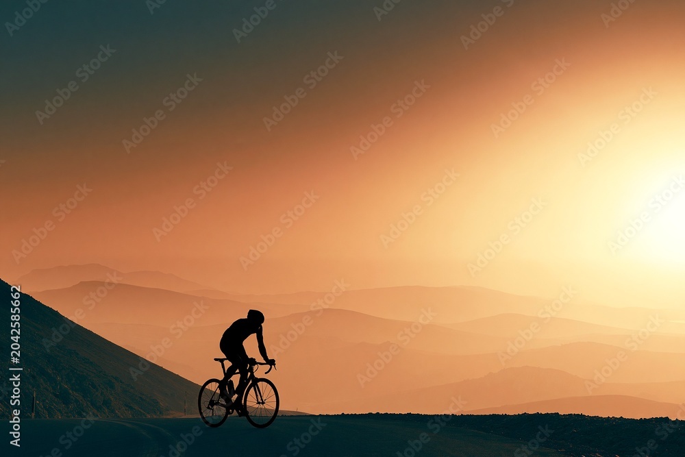 Obraz premium Lone Cyclist Riding a Mountain Pass at Hazy Dusk