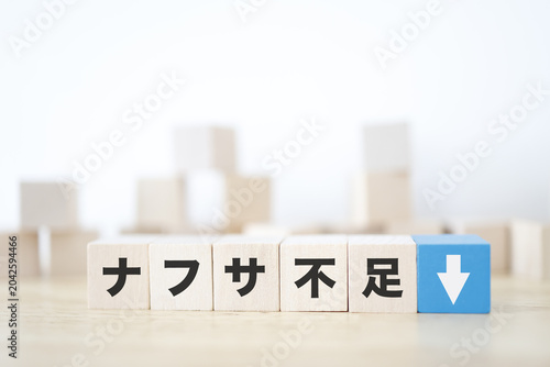 ナフサ不足。石油由来製品の供給不足。下矢印。木製ブロック。白背景