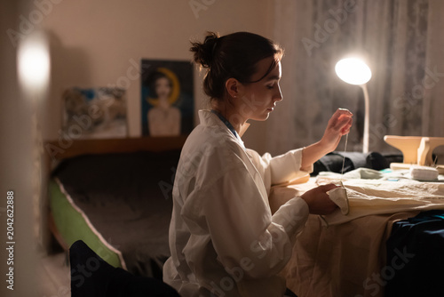 Seamstress sewing at home in lamplight