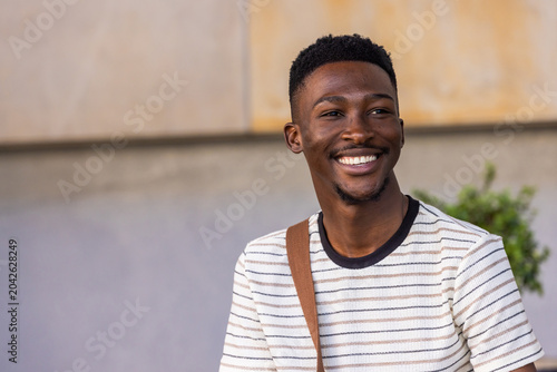 Quadro em tela African man smiling, looking right near two-tone wall wearing striped tee with b