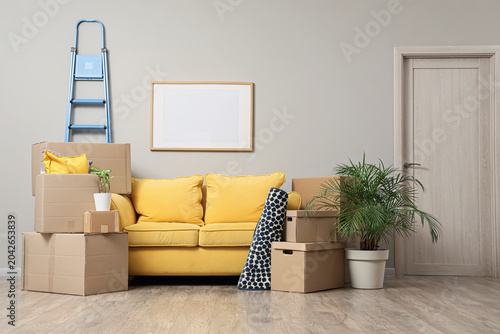 Yellow sofa with cardboard boxes and stepladder in room on moving day