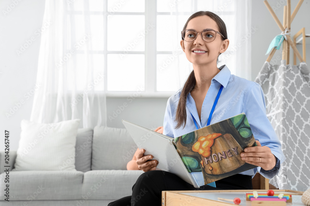Obraz premium Female nursery teacher with book sitting in kindergarten