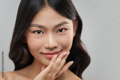 Beautiful Asian woman with flawless skin gently touches her chin