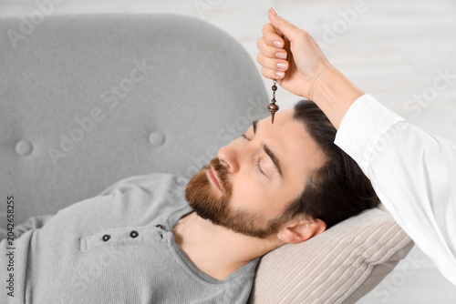 Foto Female psychologist's hand with pendulum hypnotizing man in office, closeup