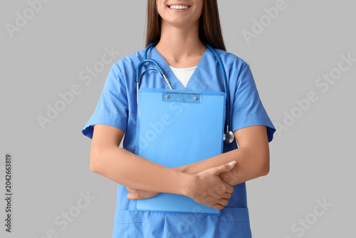 Young female doctor with clipboard on light background, closeup