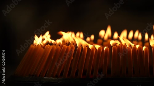 Rows of warm candle flames in a dark temple setting create a sacred visual composition with glowing light, soft smoke, and peaceful Buddhist worship atmosphere.