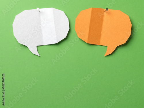 Two speech bubbles, one white and one orange, are pinned to a green background, representing communication and ideas