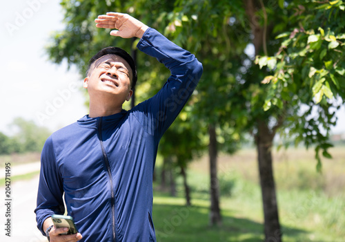Photos Portrait of a Thai man shielding his eyes from intense sunlight, showing a painful facial expression due to high heat, sunburn, or heatstroke while standing on a roadside park