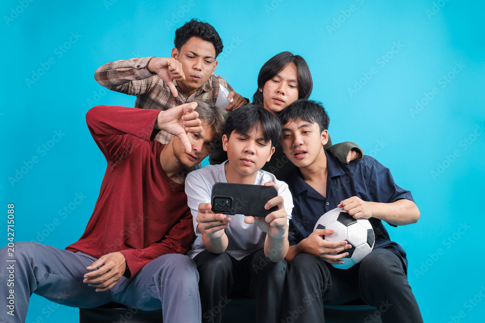 Fototapeta premium Disappointed Young Asian Men Giving Thumbs Down Gesture While Watching Losing Football Match