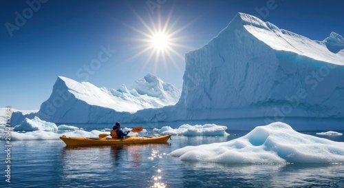 A lone kayaker paddles past giant icebergs under a bright sun