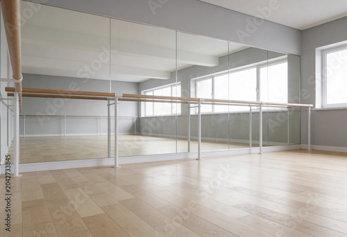 Bright minimalist barre and dance studio background. Empty fitness gym with wooden floor, full length mirrors, ballet barre, and natural light. Wellness, stretching, yoga, pilates, room interior.