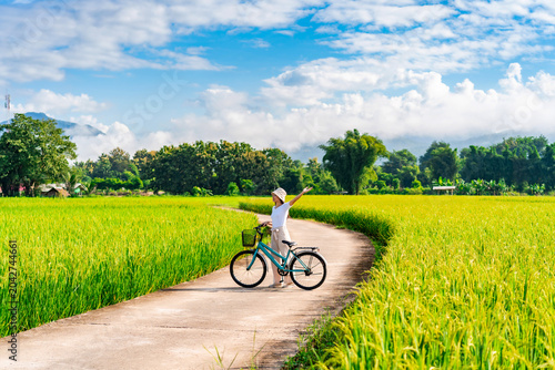 Bild auf Leinwand Young happy woman tourist enjoying and riding a bicycle in paddy field while tra