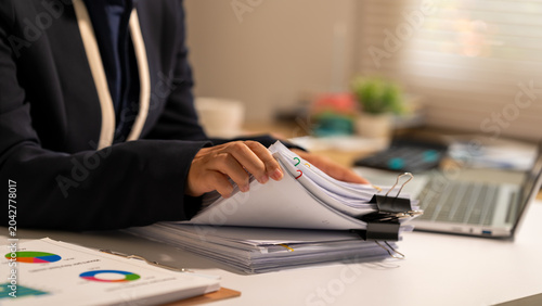 Foto Businesswoman reviewing a stack of documents at an office desk with charts, binder clips and laptop, showing paperwork, analysis and everyday administrative work